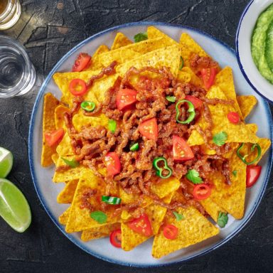 Teller mit Nachos, belegt mit Fleisch, Tomaten und Frühlingszwiebeln, serviert mit Limetten.