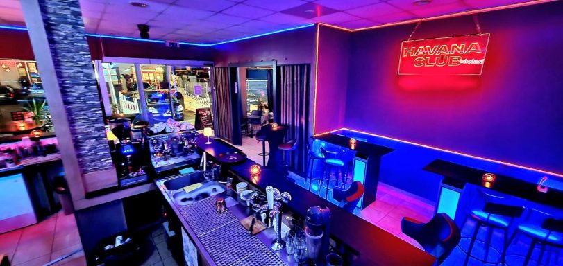 Moderne Bar mit neonfarbiger Beleuchtung und stilvollen Sitzgelegenheiten.