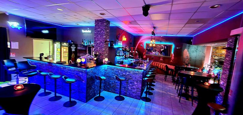 Moderne Bar mit bunten LED-Lichtern, gemütlichen Sitzbereichen und einer einladenden Atmosphäre.