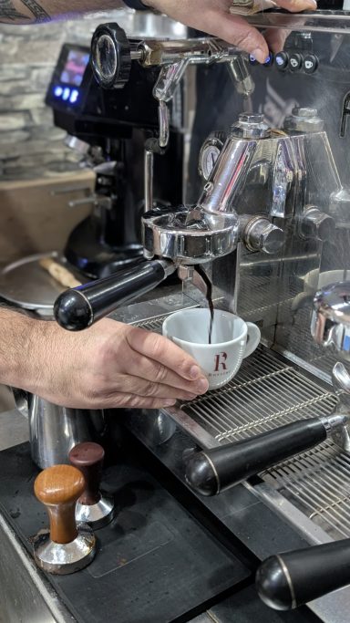 Eine Hand hält eine Tasse, während Kaffee aus einer Espressomaschine fließt.