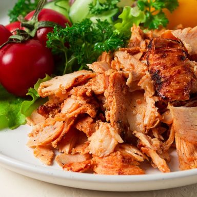 Gehäuftes gegrilltes Hähnchen mit Salat und Tomaten auf einem weißen Teller.